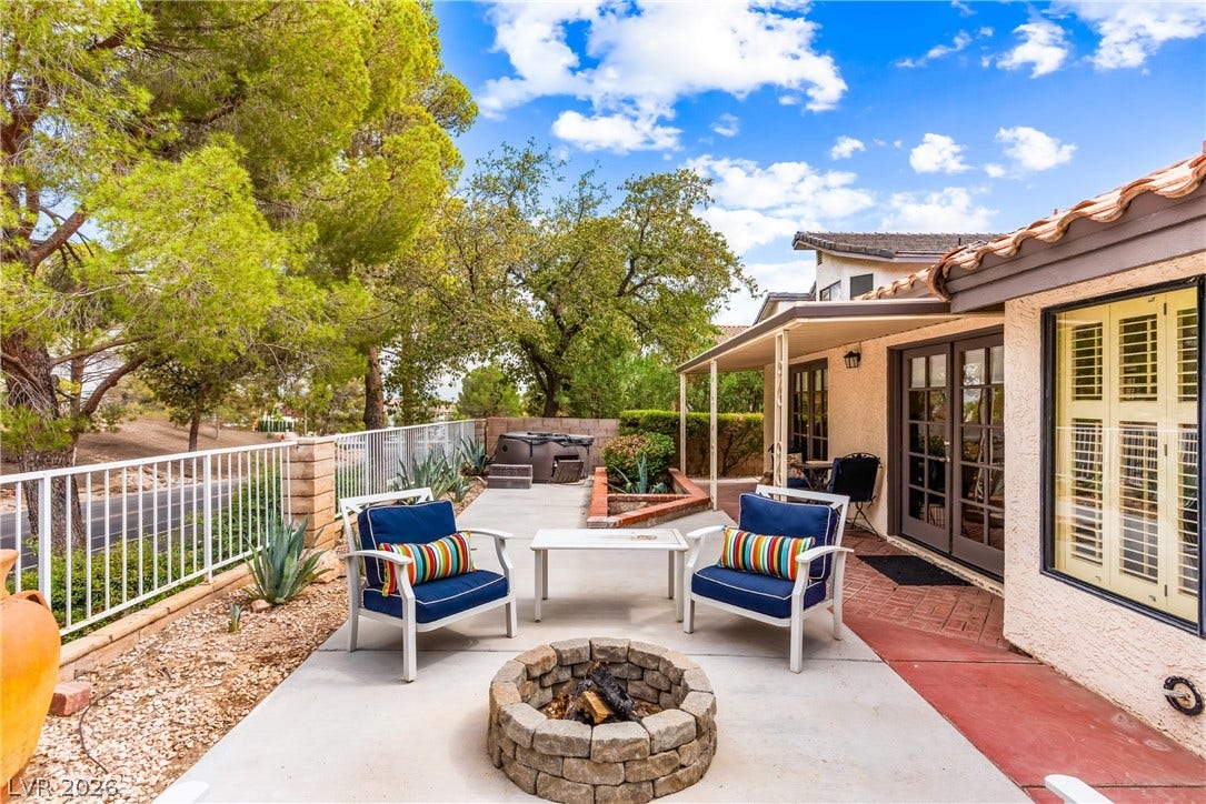 An inviting stone fire pit anchors this paved backyard patio beneath mature shade trees.