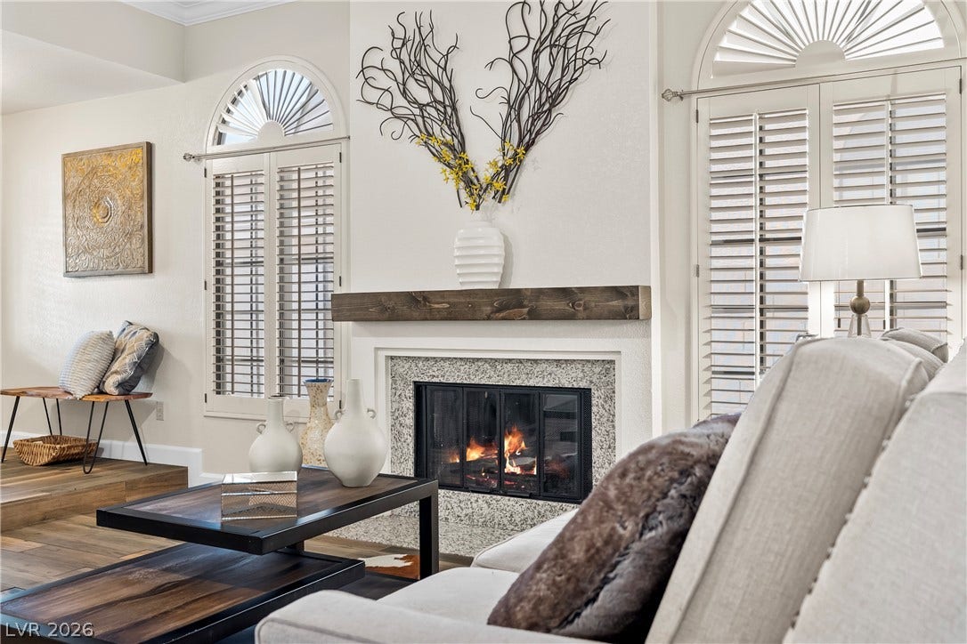 An inviting fireplace anchor the living space, framed by arched windows with plantation shutters.