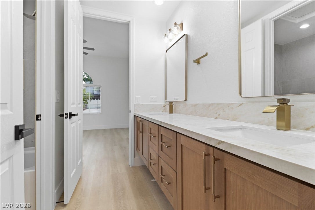 5150 Villa Dante Avenue, Las Vegas, NV 89141 Elegant brass hardware accents a spacious double vanity with stone countertops and light wood cabinetry.