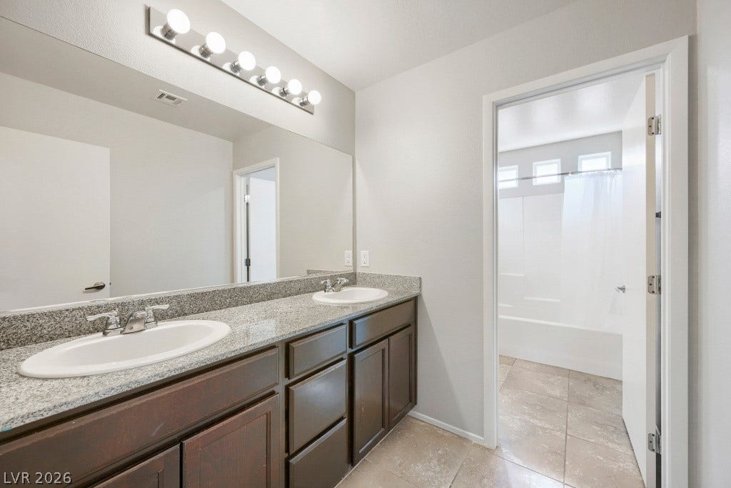 7241 Glistening Star Street, North Las Vegas, NV 89084 A stone-topped double vanity anchors this modern bathroom alongside durable tile flooring.
