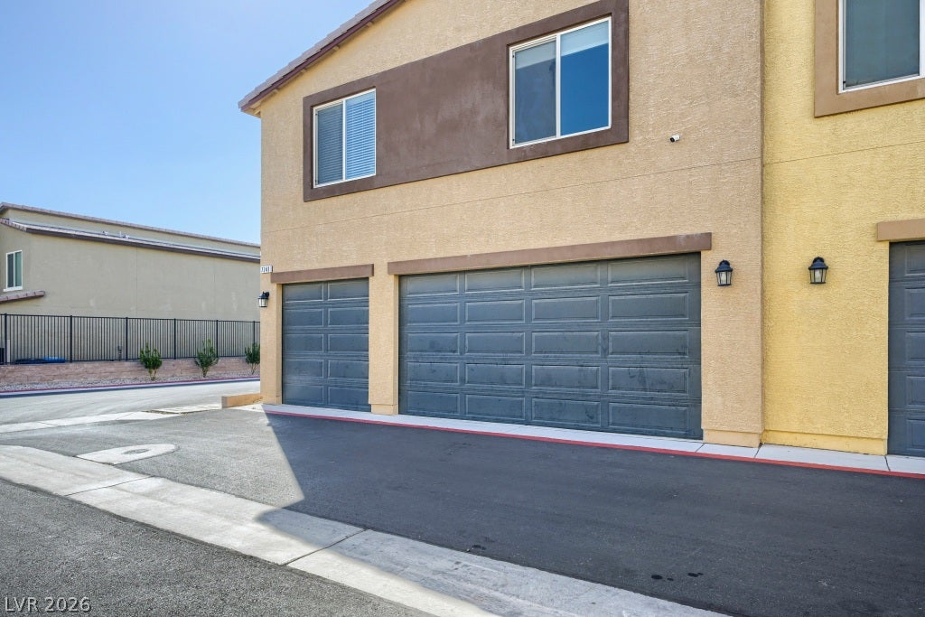 7241 Glistening Star Street, North Las Vegas, NV 89084 Multi-car garage bays sit beneath a modern stucco exterior along a paved driveway.