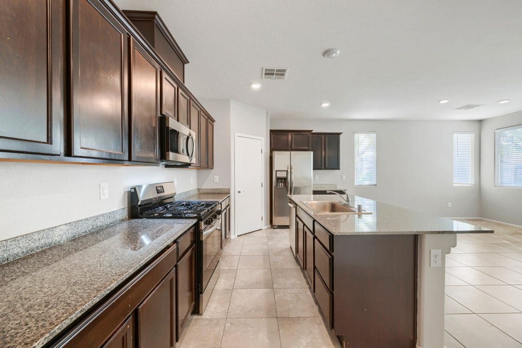 7241 Glistening Star Street, North Las Vegas, NV 89084 Rich dark wood cabinets and stone countertops anchor this functional open kitchen space.