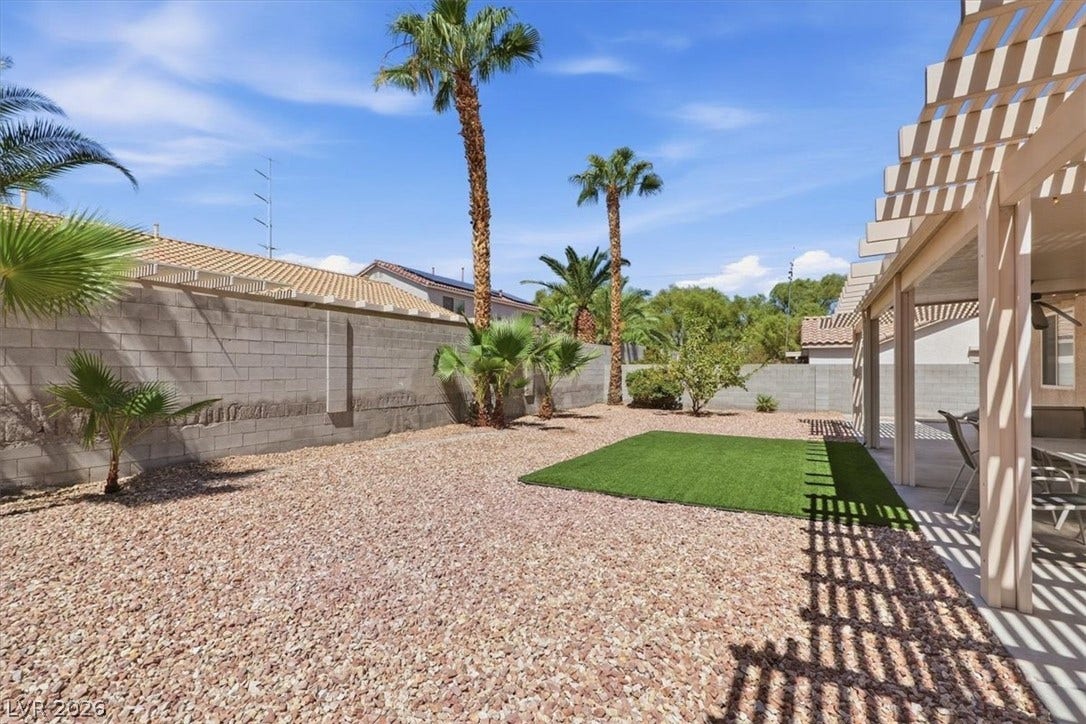 6329 Snow Cactus Street, North Las Vegas, NV 89031 Palm trees and a covered patio frame this low-maintenance gravel yard with a block wall.