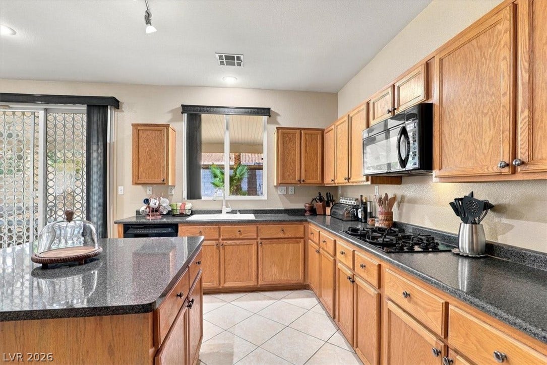 6329 Snow Cactus Street, North Las Vegas, NV 89031 Ample wooden cabinetry and dark stone countertops anchor this classic kitchen space.