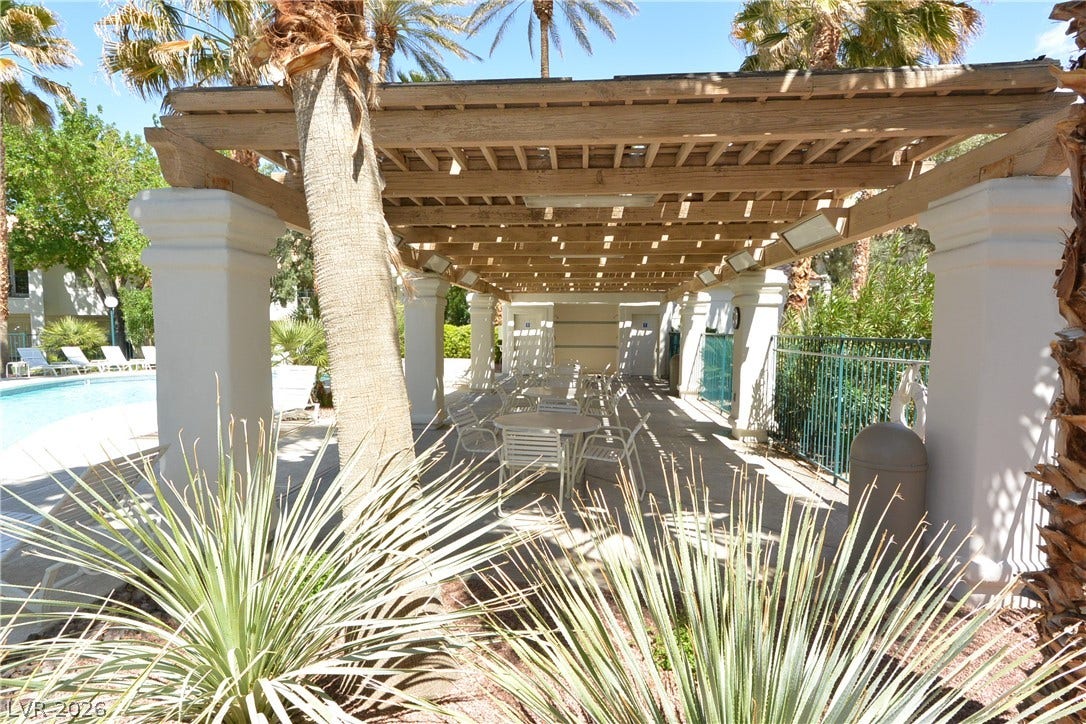 A spacious poolside pergola provides shaded seating among palm trees.