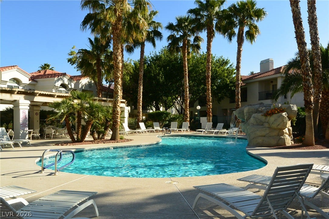 Palm trees flank a pristine community swimming pool surrounded by paved lounging areas.