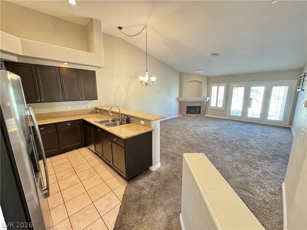 An open floorplan connects the tiled kitchen directly to a carpeted living area with fireplace.
