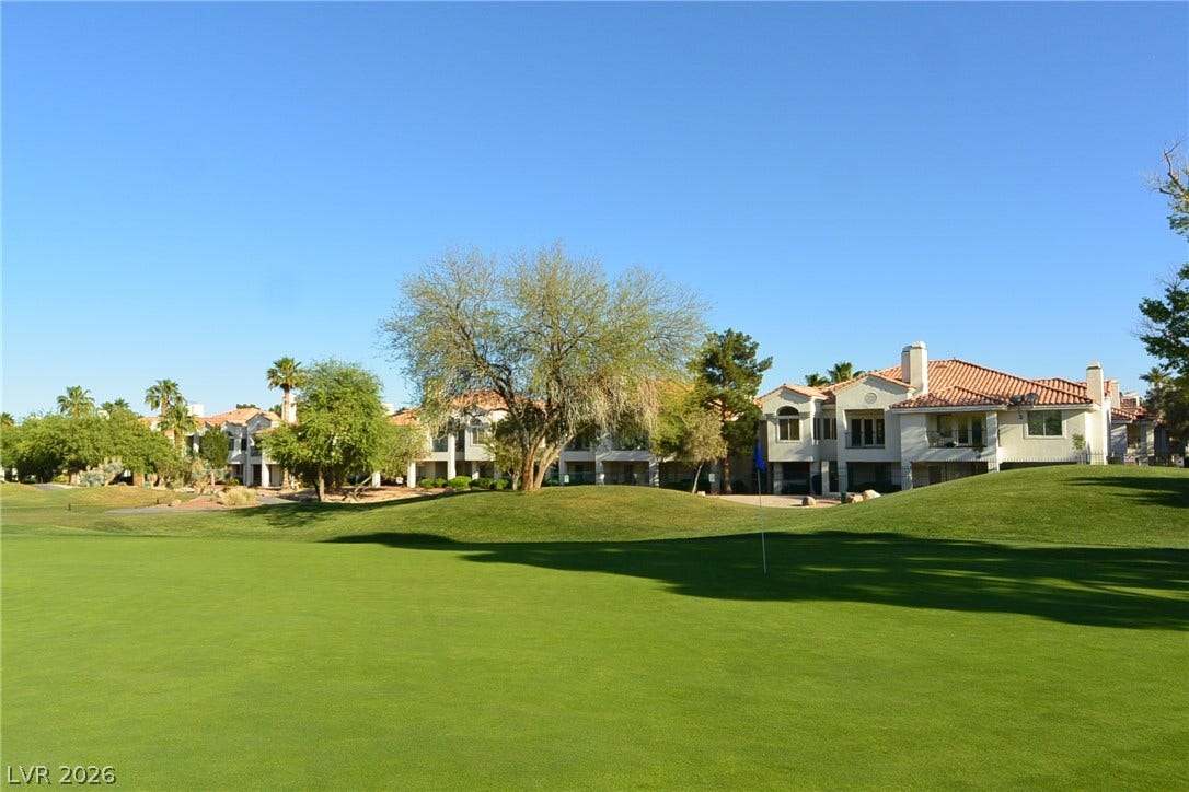 Lush fairways stretch toward tiled-roof residences under a clear blue sky.
