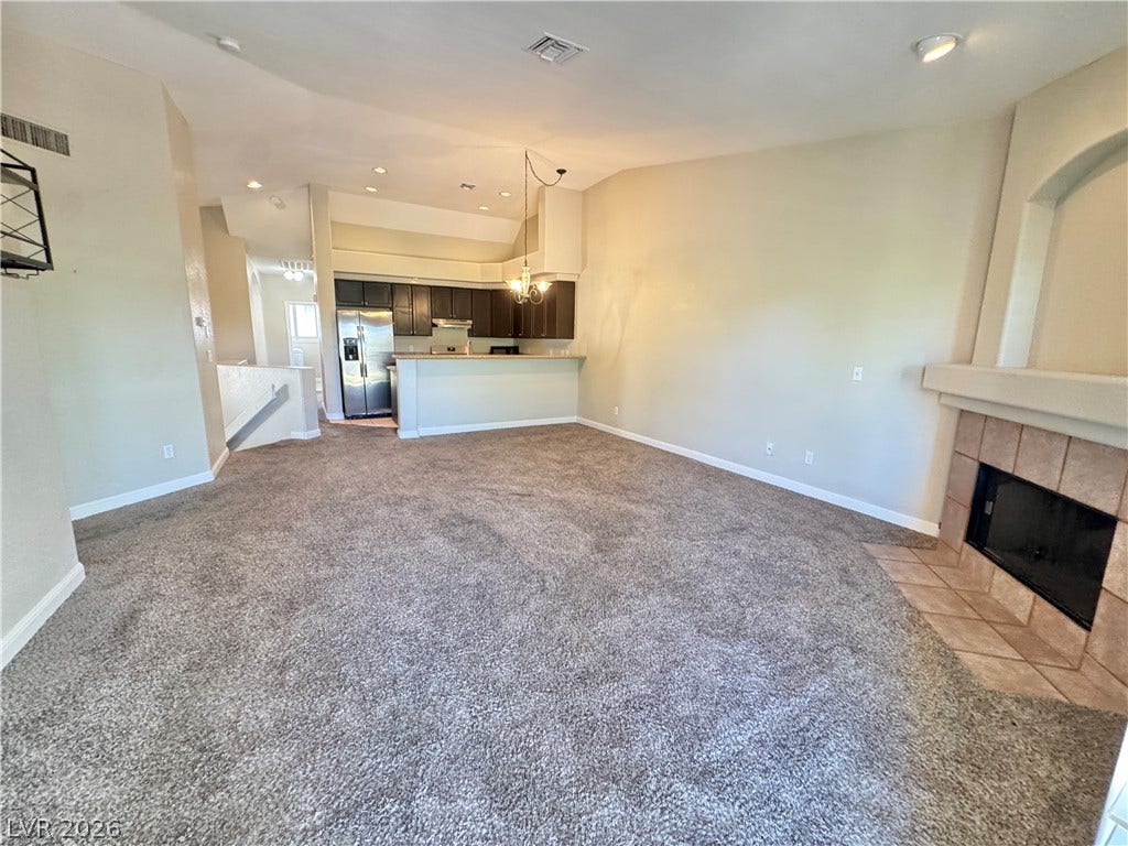 A spacious living area connects seamlessly to the kitchen and features a tiled fireplace hearth.