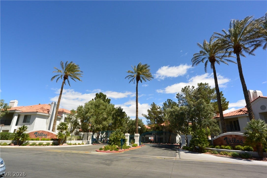 Stately palm trees frame the gated community entrance under a bright blue sky.