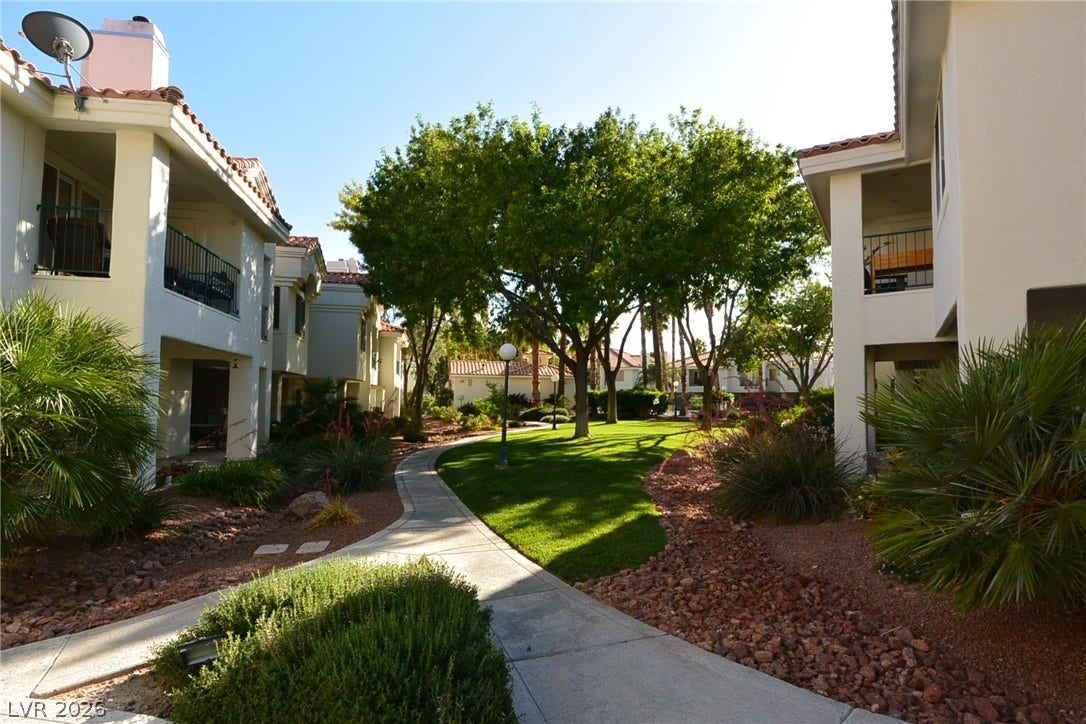 Manicured green pathways wind between elegant stucco residential structures under a clear sky.