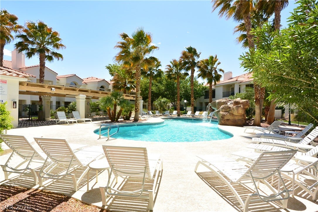 Palm trees frame a sparkling community pool featuring a rocky waterfall feature.