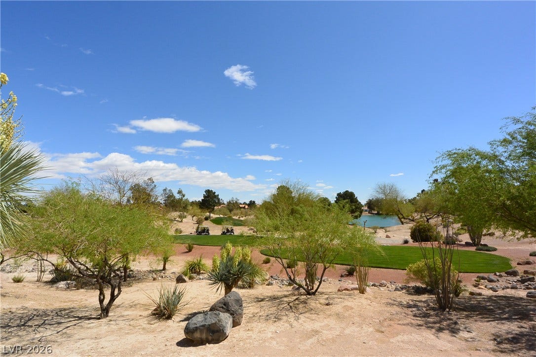 Lush desert landscaping frames panoramic views of the verdant golf course and distant water feature.