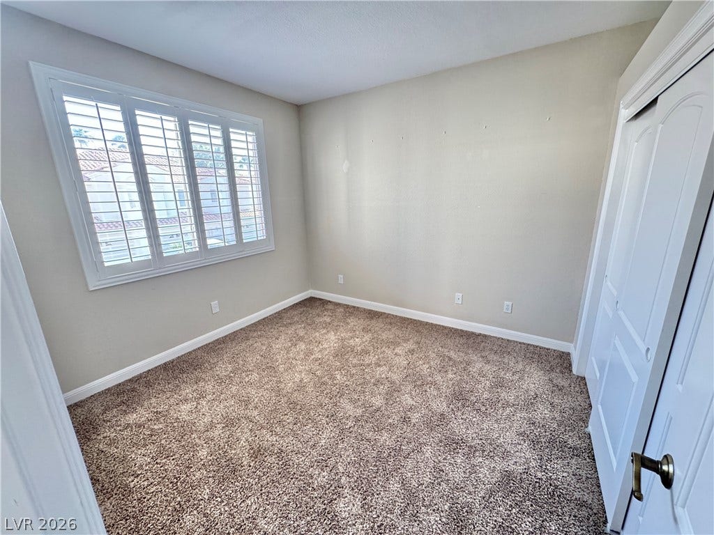 A window with plantation shutters brings natural light into this carpeted bedroom.