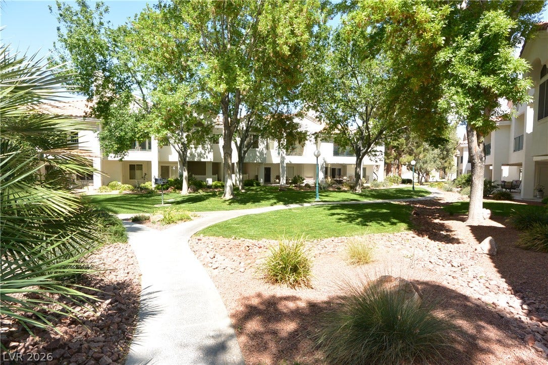 Mature trees shade paved walking paths weaving through a beautifully landscaped green common area.