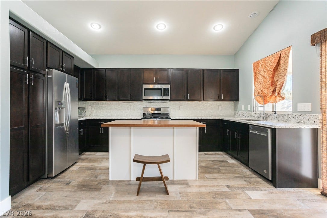 2421 Sunrise Springs Court, North Las Vegas, NV 89031 Rich dark cabinetry contrasts with a central island and light plank flooring in this spacious kitchen.