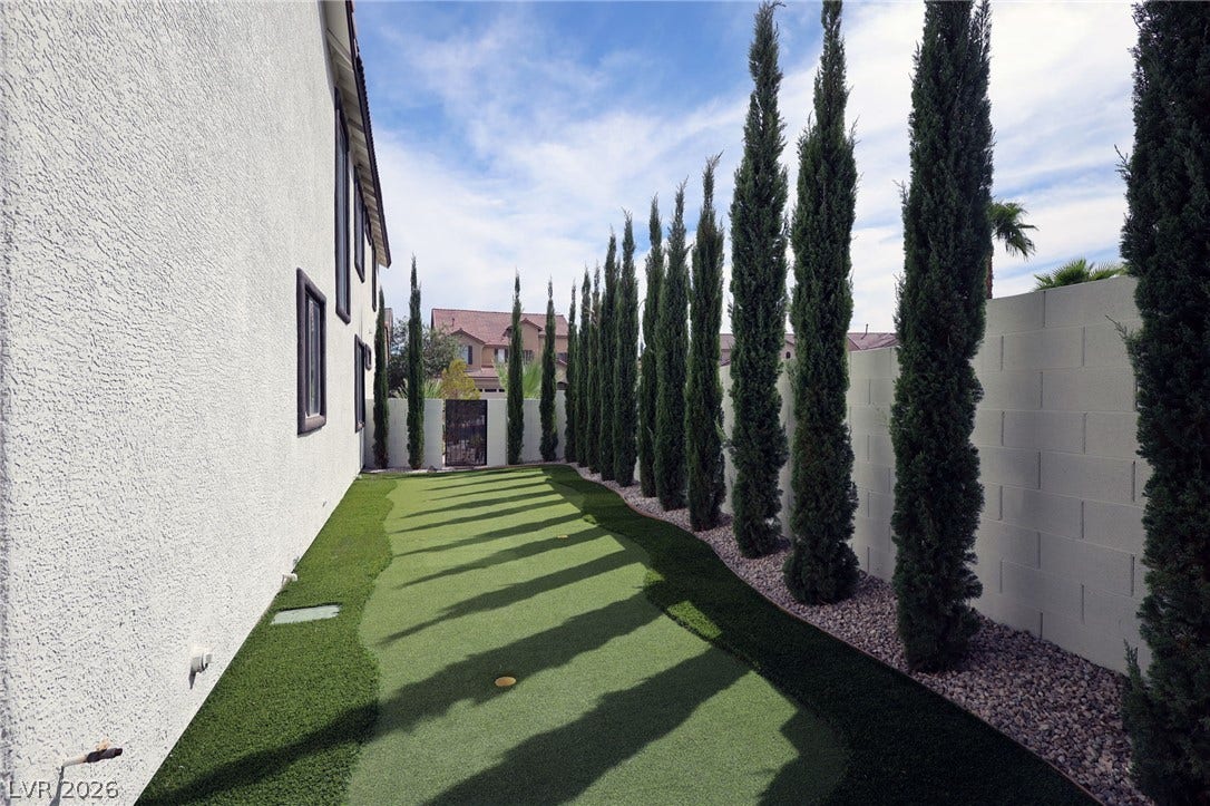 3018 Via Sarafina Drive, Henderson, NV 89052 A private putting green runs alongside the stucco exterior under a line of tall cypress trees.