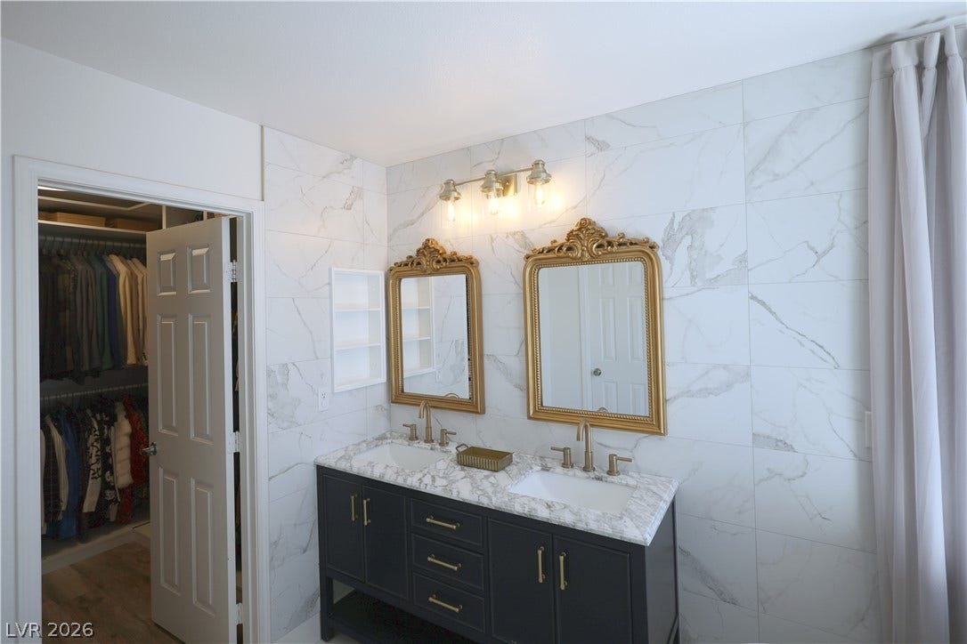 3018 Via Sarafina Drive, Henderson, NV 89052 Ornate gold mirrors accent a double vanity against an elegant marble tile wall.