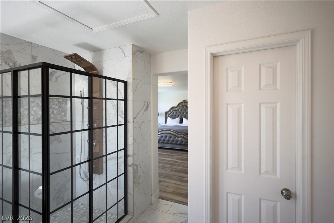 3018 Via Sarafina Drive, Henderson, NV 89052 An elegant marble-tiled walk-in shower features modern black framing next to the main suite entryway.
