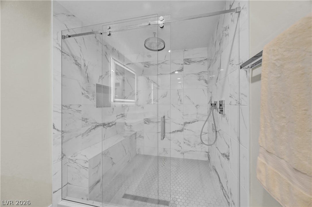 4709 Amazing View Street, Las Vegas, NV 89129 Floor-to-ceiling marble-patterned tile surrounds a spacious glass-enclosed shower featuring built-in bench seating.
