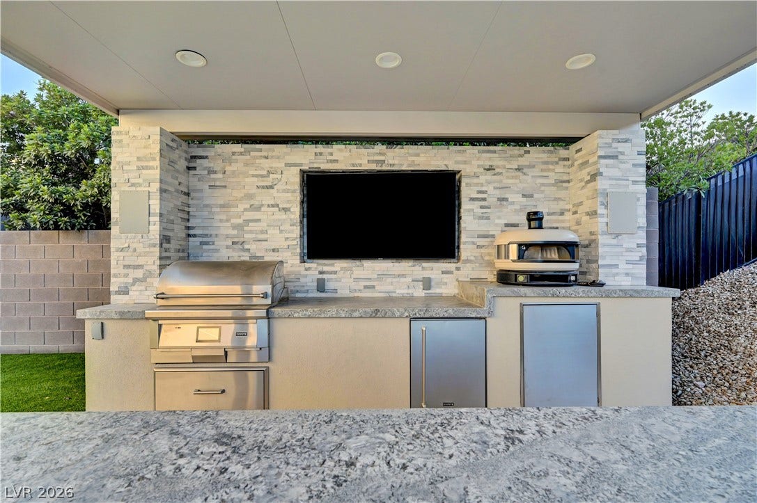 4709 Amazing View Street, Las Vegas, NV 89129 An covered outdoor kitchen features polished stone countertops and a stacked stone accent wall.
