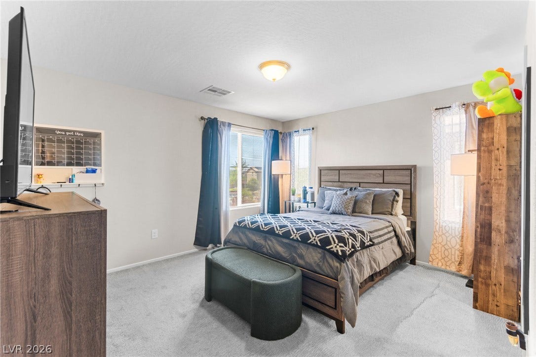 7224 Halo Falls Street, North Las Vegas, NV 89084 A restful chamber offers soft gray carpet, a spacious bed with a patterned throw, and a pair of large windows that usher in natural light.
