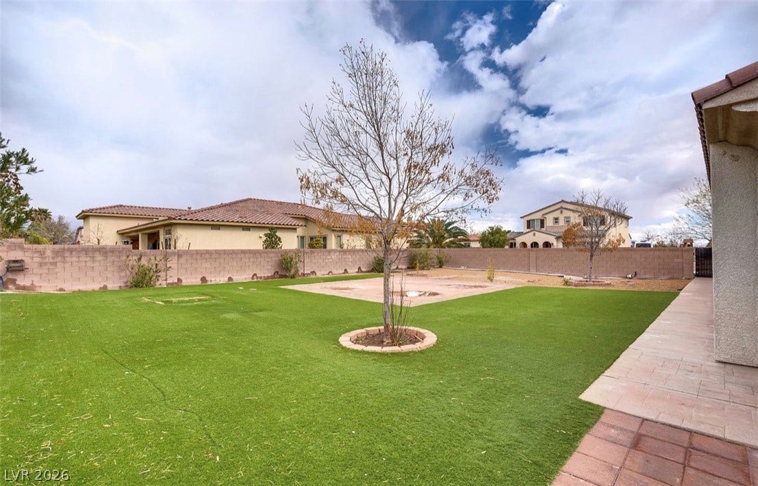 4709 Estate Ranch Street, North Las Vegas, NV 89031 A spacious backyard features an expanse of green turf, bordered by a privacy wall and a mature tree.