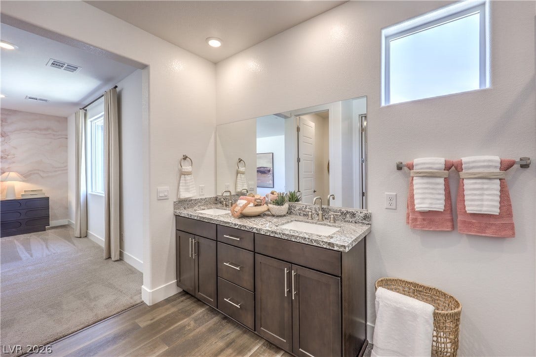 844 Kassie Lake Way, North Las Vegas, NV 89084 A stone-countertop double vanity sits beneath a large mirror and recessed lighting. Representational only; Photo is of the 2660 Plan Model Home - NOT THE ACTUAL HOME FOR SALE *material/features/colors can vary from one community to the next & are subject to change*