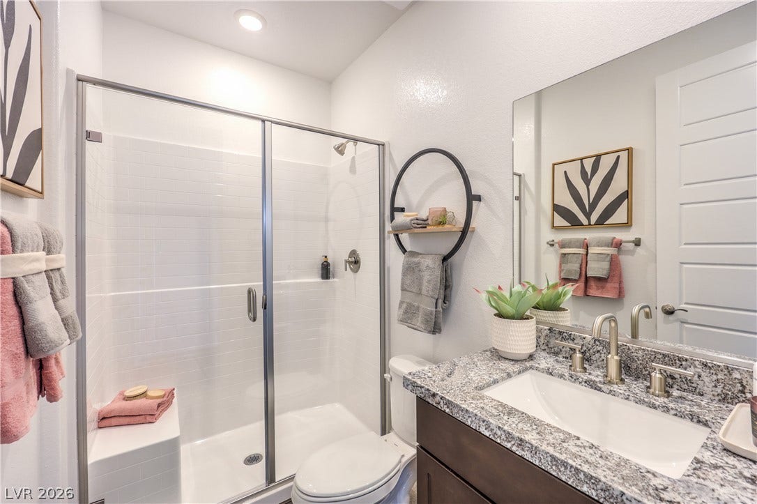 844 Kassie Lake Way, North Las Vegas, NV 89084 Polished stone counters elevate this contemporary bathroom featuring a spacious glass-enclosed shower. Representational only; Photo is of the 2660 Plan Model Home - NOT THE ACTUAL HOME FOR SALE *material/features/colors can vary from one community to the next & are subject to change*