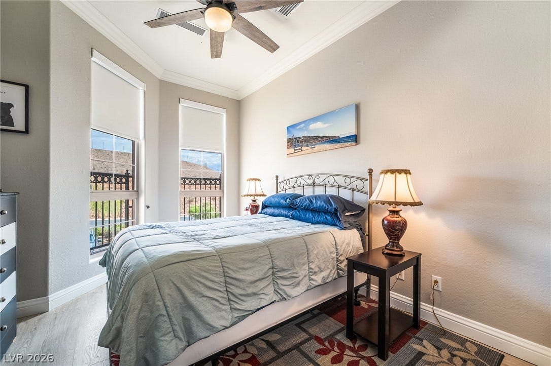 30 Via Vasari, #103, Henderson, NV 89011 Crown molding and tall windows frame this comfortable bedroom with wood-look flooring.