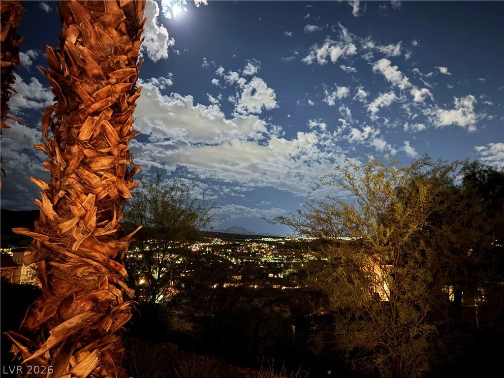 30 Via Vasari, #103, Henderson, NV 89011 Glittering city lights shine beneath a dramatic night sky framed by natural desert landscape.