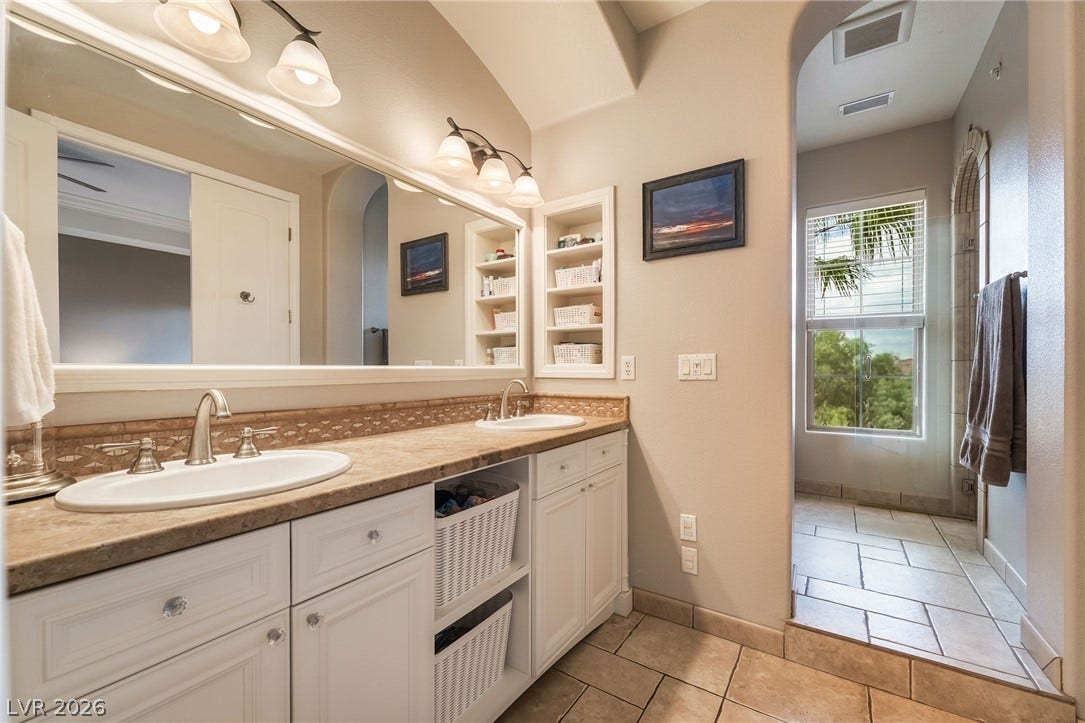 30 Via Vasari, #103, Henderson, NV 89011 Double vanity sinks and built-in shelving complement the tiled floors and walk-in shower access.