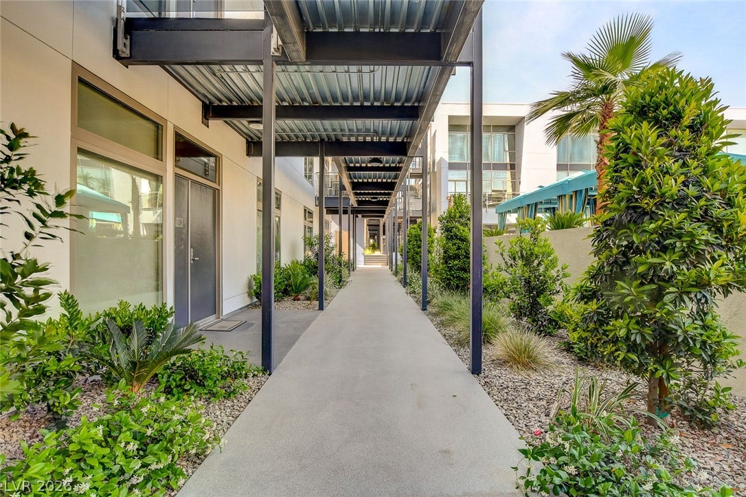 8925 W Flamingo Road, #111, Las Vegas, NV 89147 A covered concrete walkway runs alongside modern stucco residences lined with manicured landscaping.