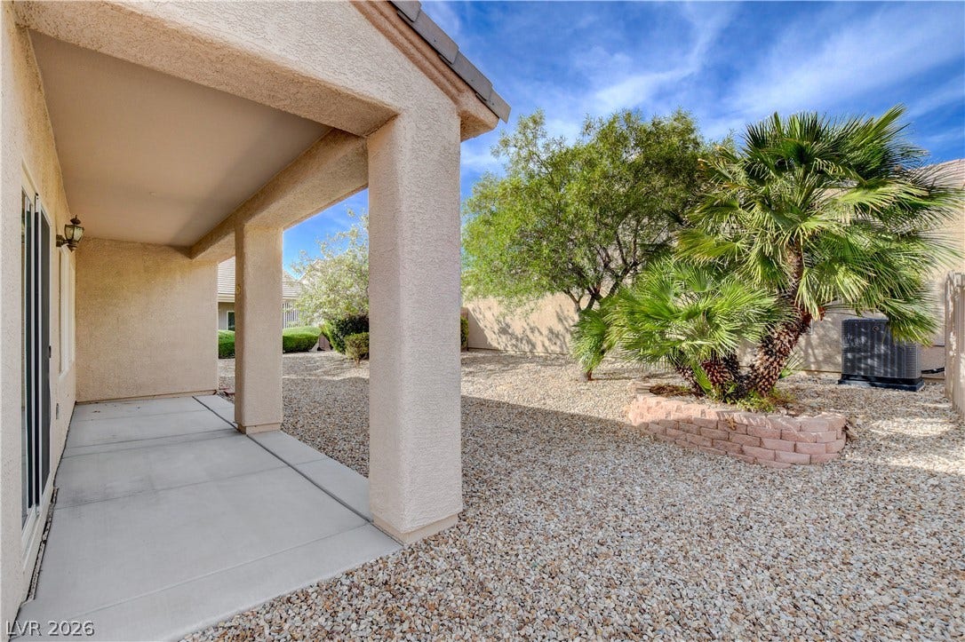 2612 Rock Pigeon Avenue, North Las Vegas, NV 89084 A covered concrete patio overlooks a low-maintenance gravel yard with mature palm trees.