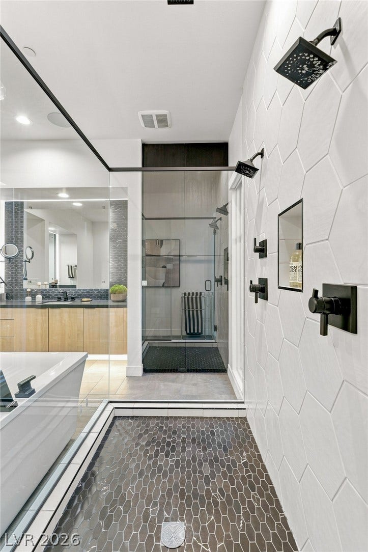 A spacious walk-in shower features geometric wall tiling and modern matte black fixtures.