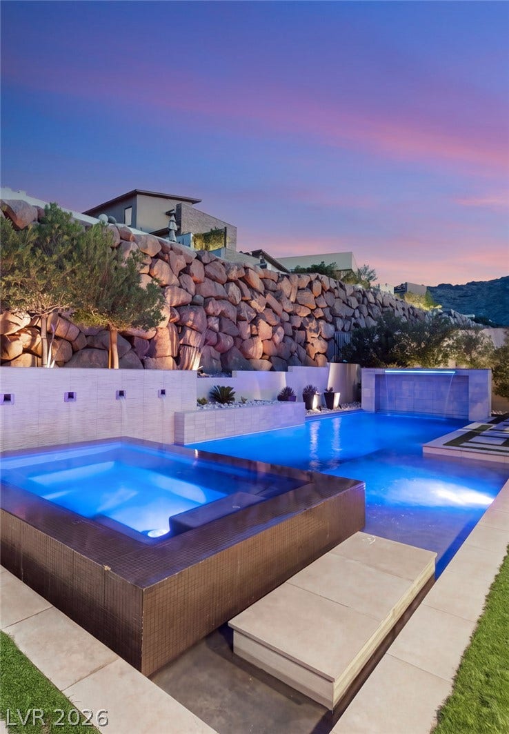 A stone retaining wall rises behind a modern geometric pool and integrated spa.