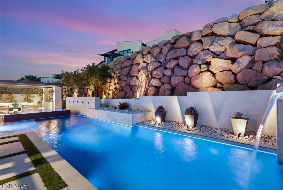 An inviting swimming pool borders a dramatic stone retaining wall set against a twilight sky.