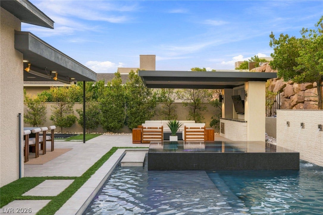 An inviting backyard oasis features a modern swimming pool and a covered patio kitchen.