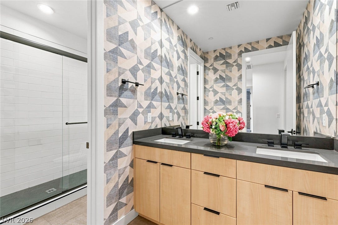 A contemporary bathroom features a double vanity with stone counters and geometric wall coverings.
