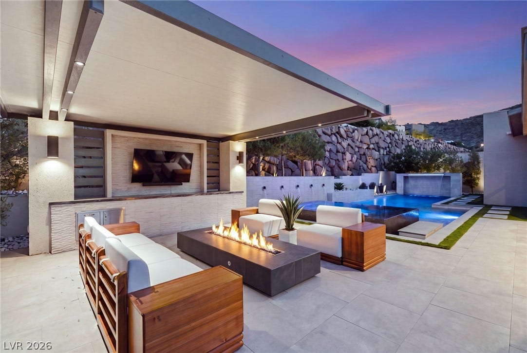 An covered patio with recessed lighting leads seamlessly to a poolside lounge and fireplace.
