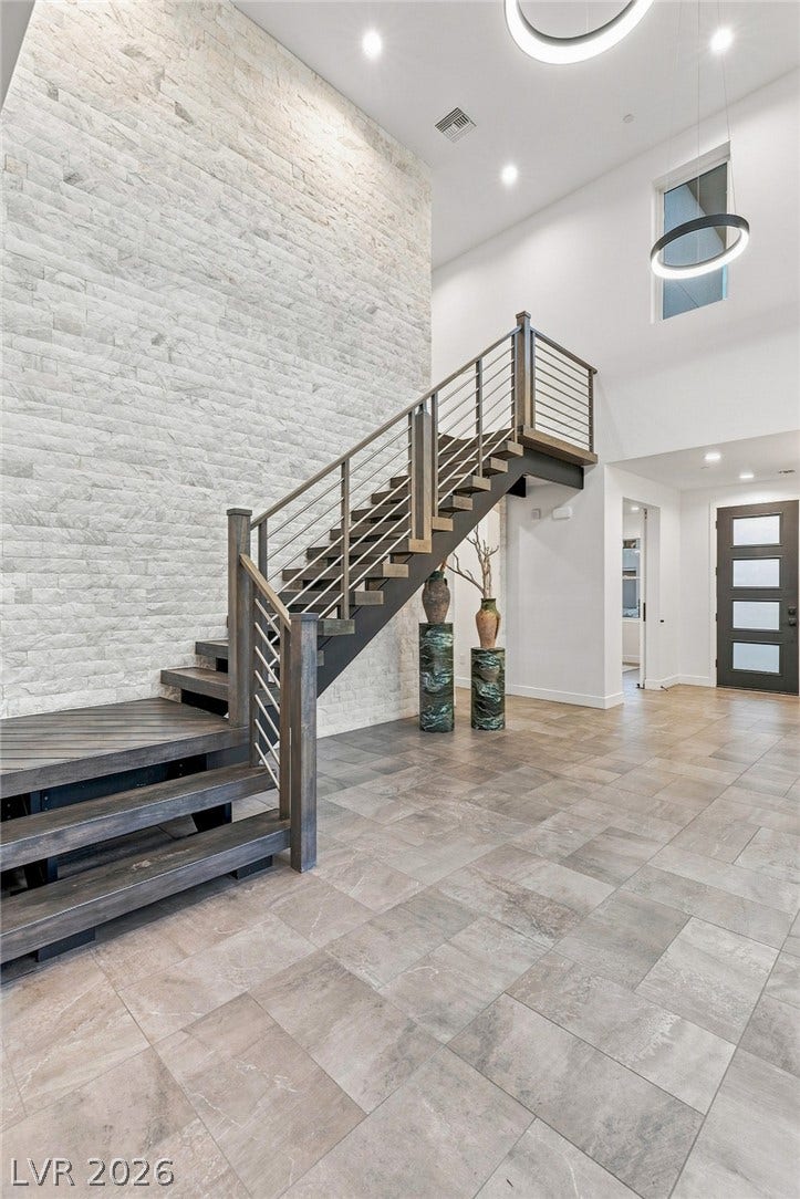Soaring ceilings and an architectural stone wall frame a dramatic modern staircase.