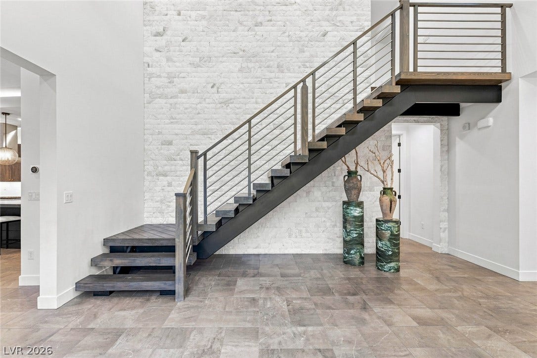 A modern staircase ascends against a textured stone wall, complemented by tile flooring.