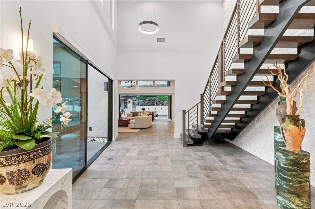 An open entry foyer features tile flooring, towering ceilings, and a modern open-tread staircase.