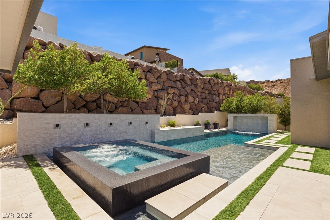 An custom swimming pool and integrated spa sit nestled against a dramatic rock retaining wall.