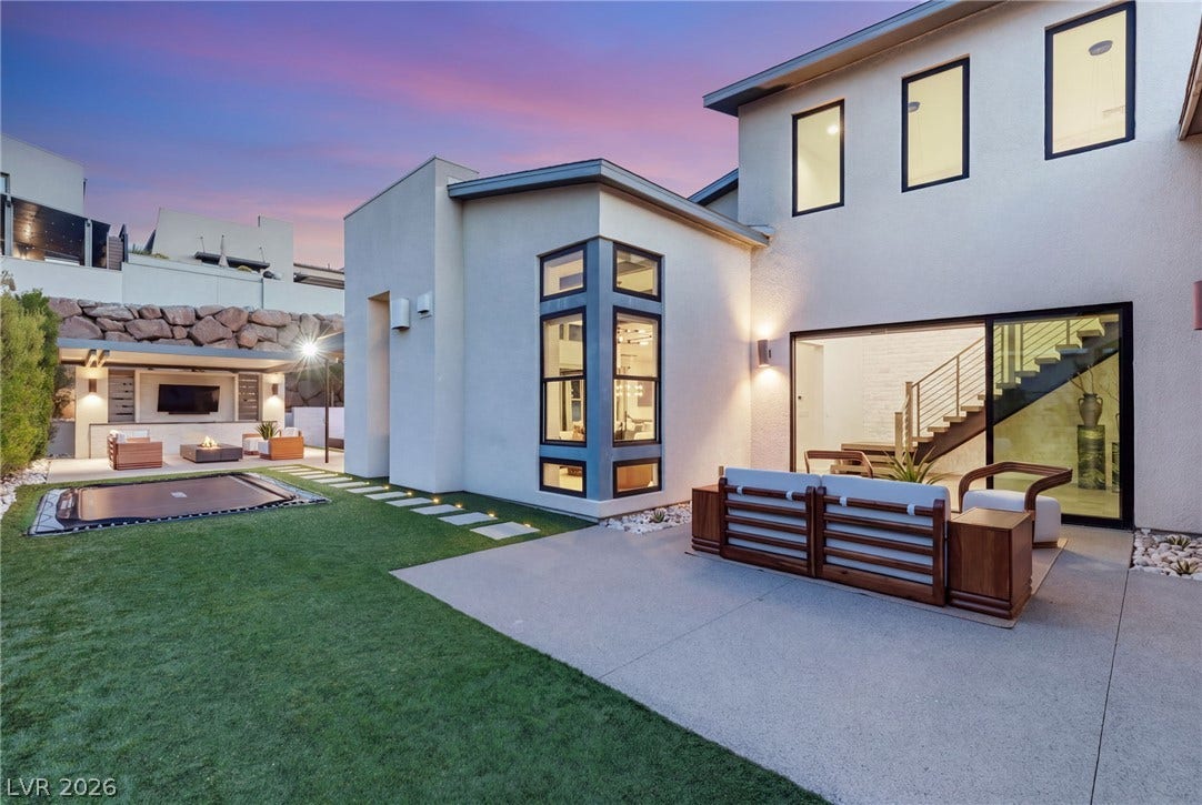 Geometric modern architecture frames a concrete patio, stone steps, and an expansive lawn.