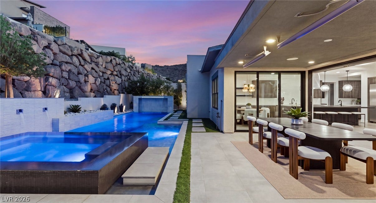 A spacious covered patio seamlessly transitions to a luxury pool and spa area below terraced stone walls.