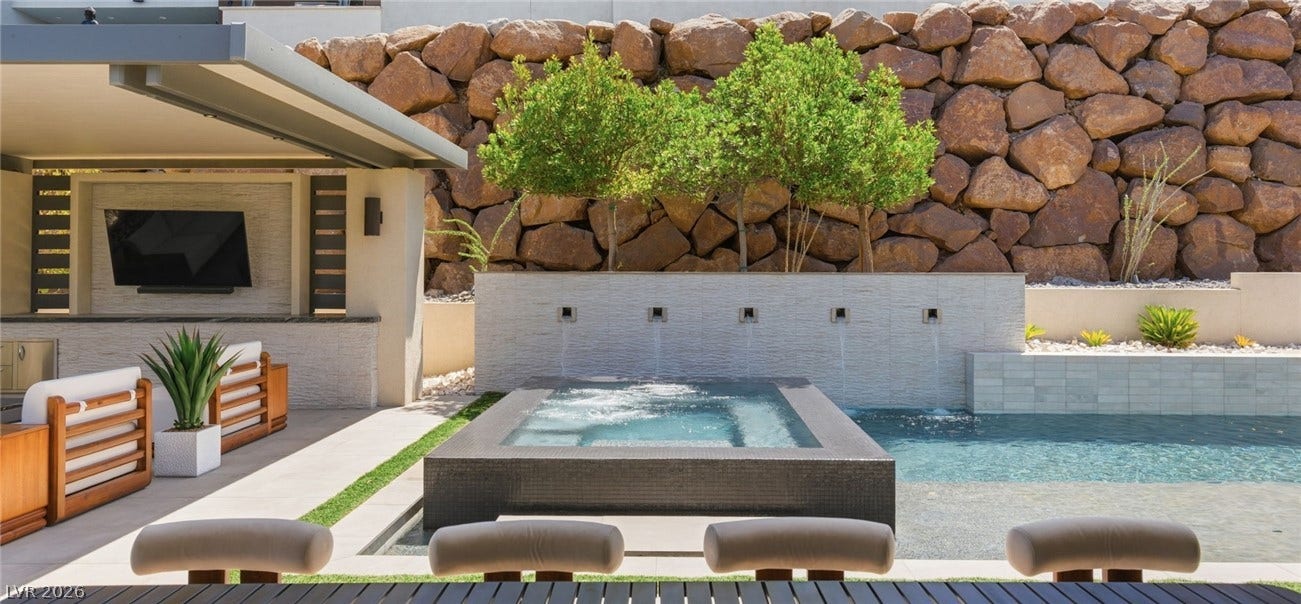 An integrated spa overflows into the swimming pool beneath a custom stone retaining wall.