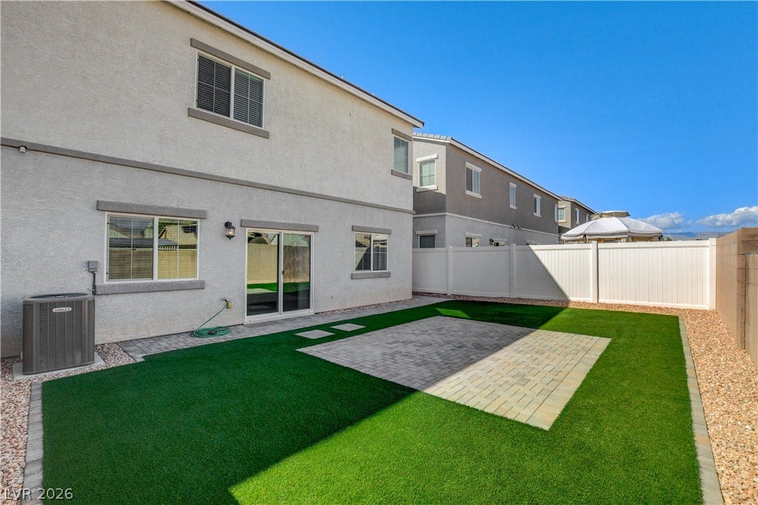 A neat paved patio is surrounded by artificial turf in this low-maintenance fenced backyard.