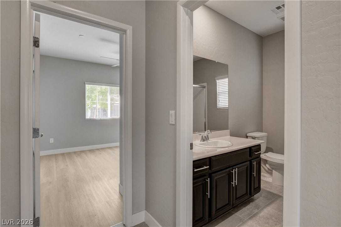 A modern vanity sits adjacent to a bedroom finished with durable wood-look flooring.