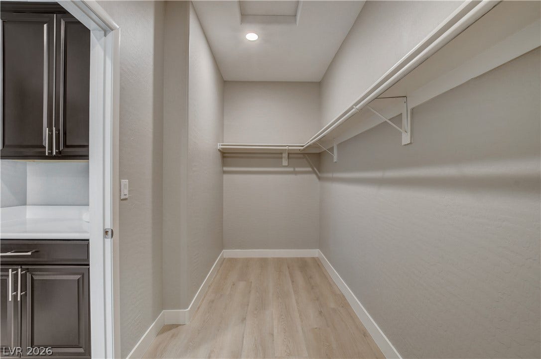 A spacious walk-in closet features built-in shelving, recessed lighting, and durable wood-look flooring.